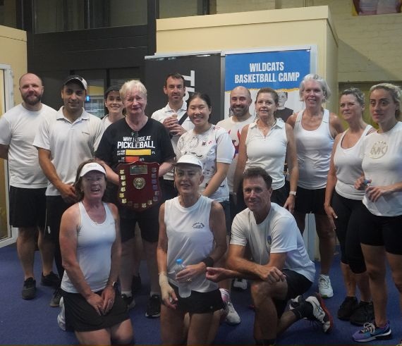 Club members gathered indoors with a player holding a large trophy shield