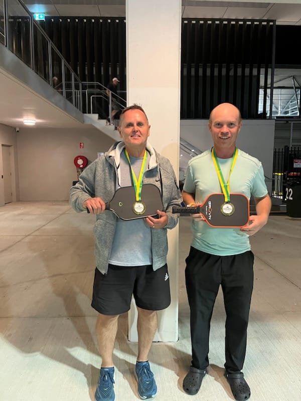 Two club members holding paddles with medals after a competition