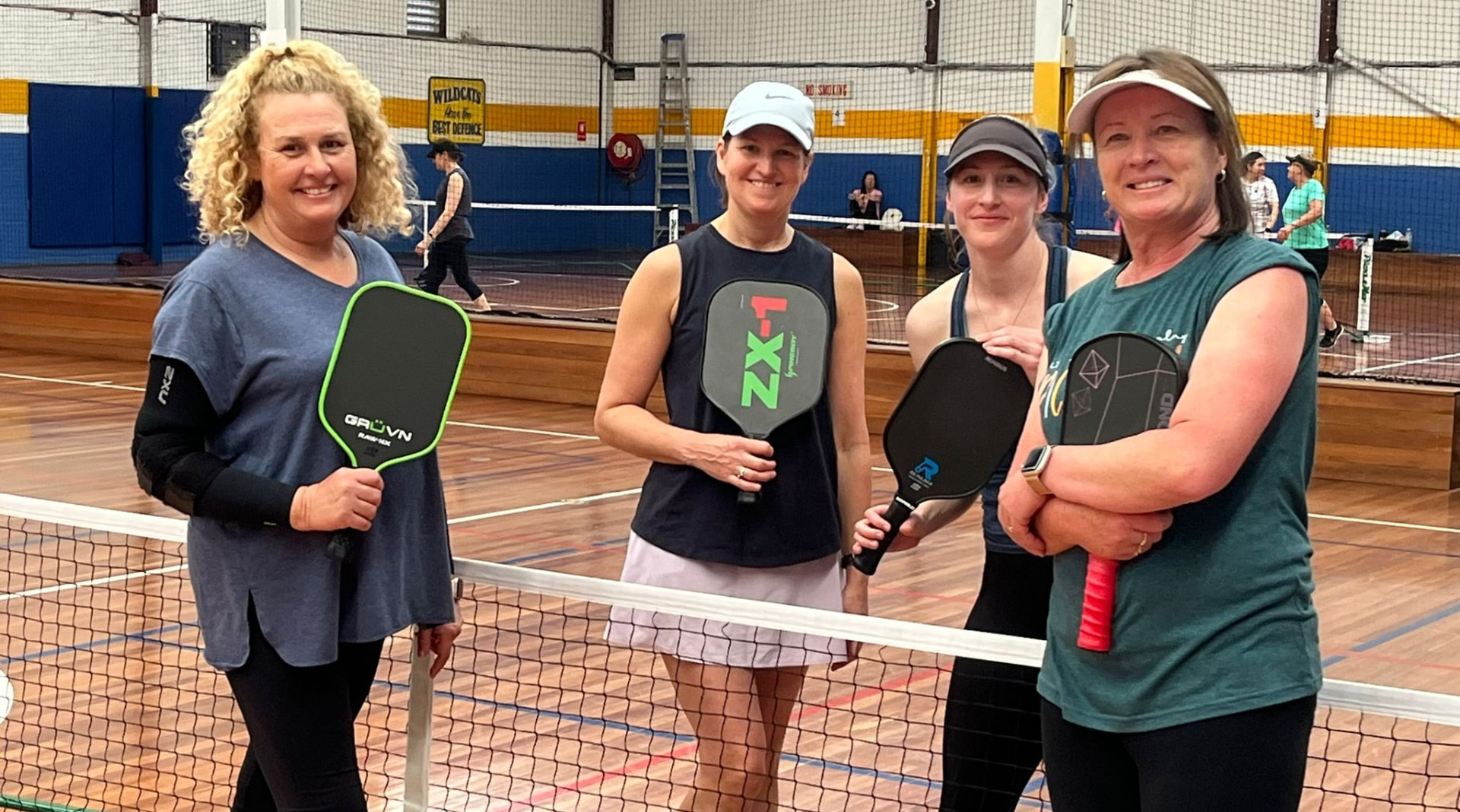 Four members with their paddles gathered at the net indoors