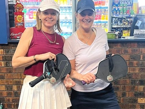 Two club members proudly holding paddles with medals after a competition