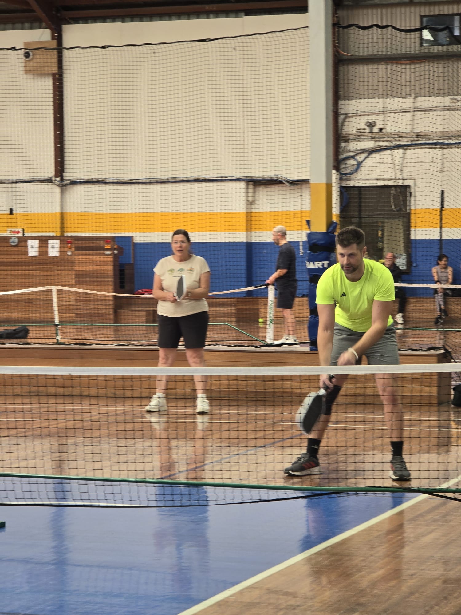 Mixed doubles partners positioned at the net during an indoor session