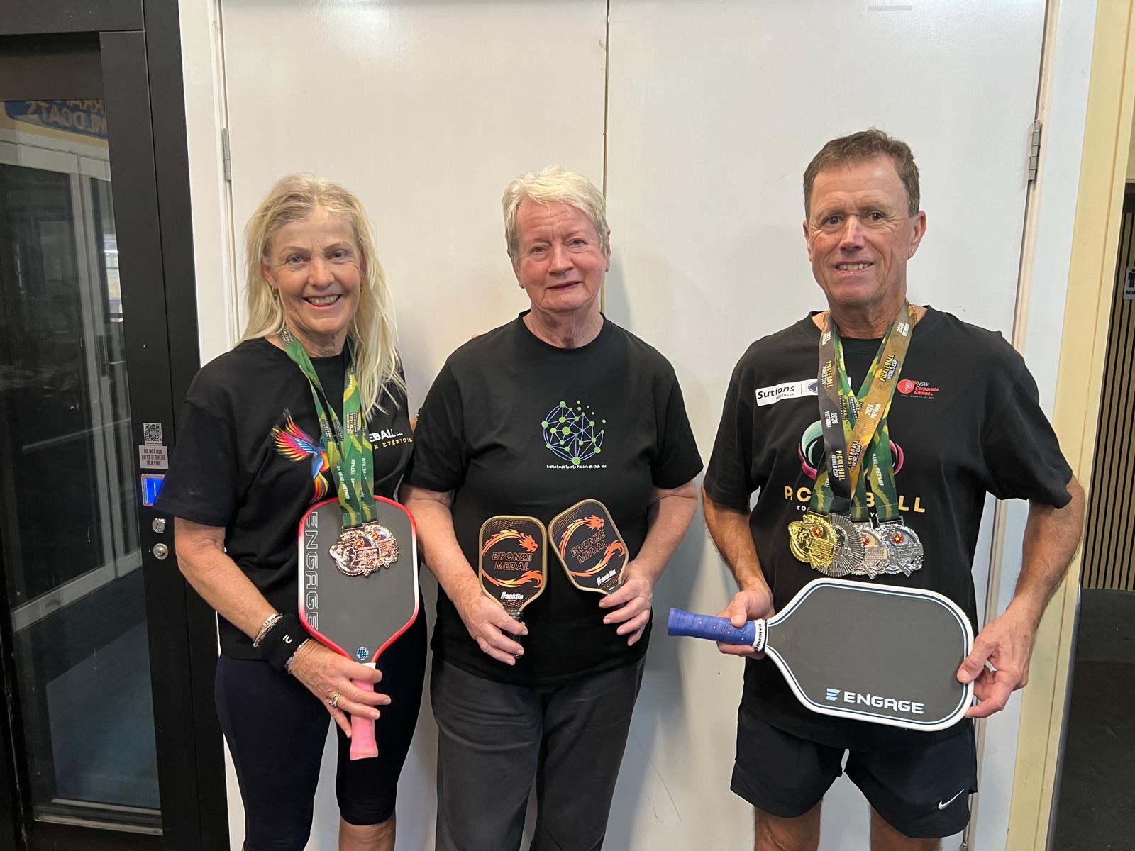 Three club members showing their medals and paddles after a competition