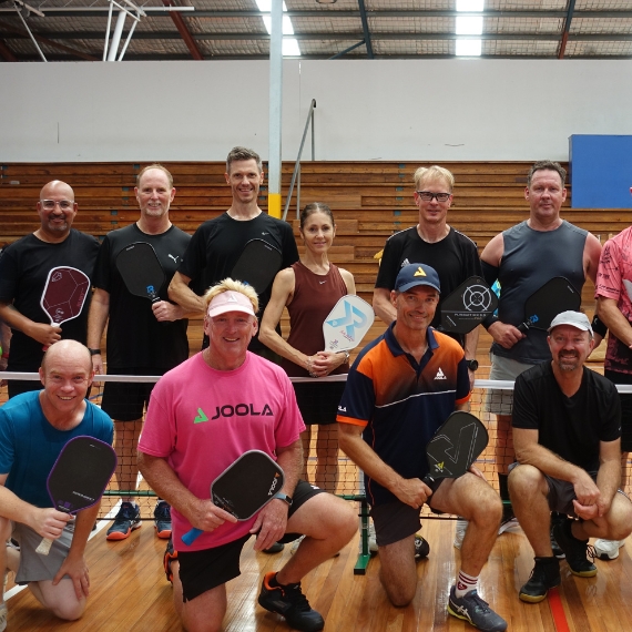 A group of club members with their paddles gathered around the net